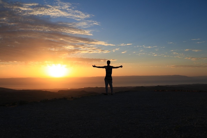 Person standing with arms open in front of a sunset
