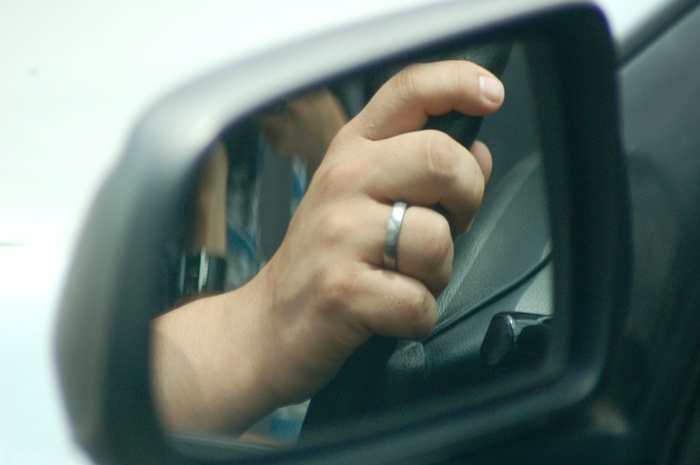 Person's hands on car steeling wheel from the view of the side mirror