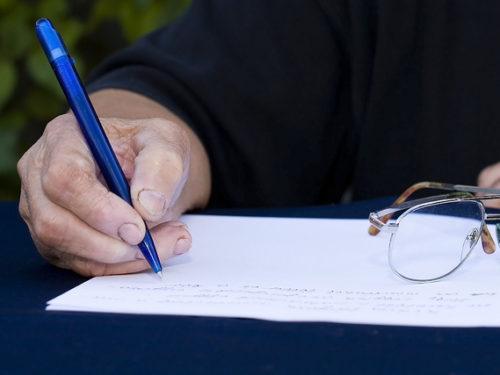 Person writing something on paper with a blue pen