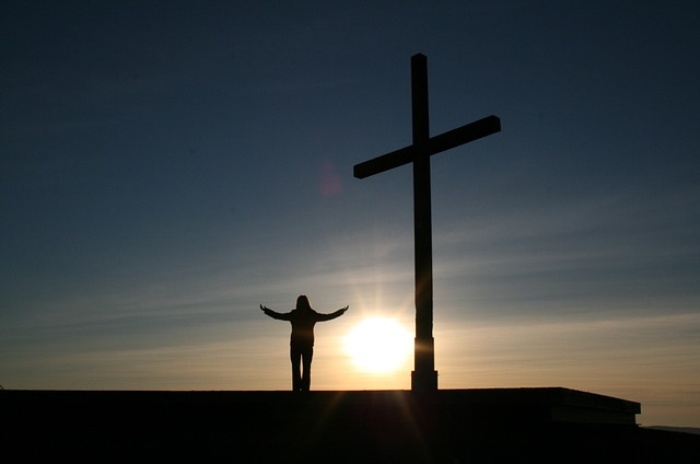 Person standing on roof with cross and sun setting in the back