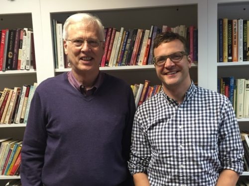 Two men standing next to each other in front of a bookcase
